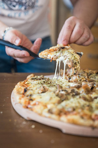 男人在木桌上切块正宗的自制奶酪披萨