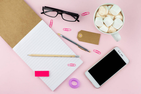 创意平面照片的工作空间办公桌与智能手机眼镜笔铅笔和笔记本最小风格的粉红色背景。 最低业务概念
