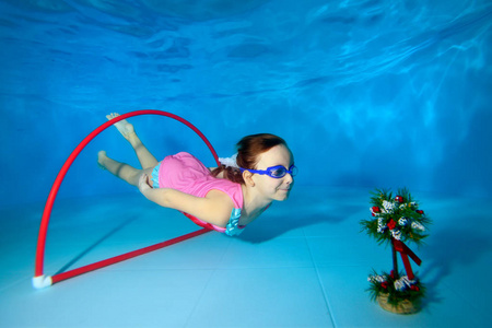 这孩子在水下玩运动。 潜水和游泳通过游泳池底部的箍。 肖像。 水平方向。 从水下看到的景色