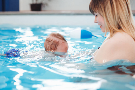 白种人的母亲把她新生的婴儿转移到游泳池里漂浮。 婴儿在水里潜水。 健康活跃的生活方式。 家庭活动和早期发展概念