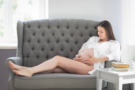 年轻俏丽的怀孕的妇女坐在沙发上在室内