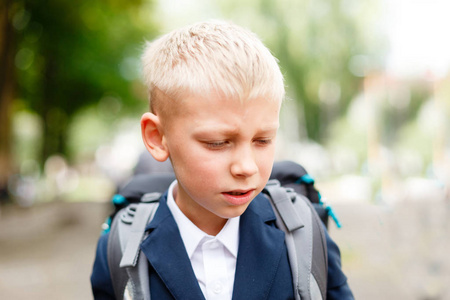悲伤和不快乐的孩子在学校背景上带着书包。