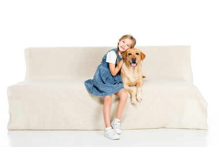 微笑的孩子和狗坐在沙发上，被孤立在白色上