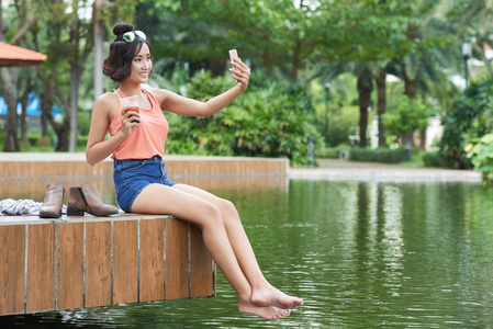 年轻女子坐在公园池塘里自拍