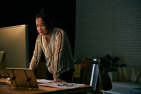 印尼商界女性在黑暗办公室的电脑屏幕上阅读信息