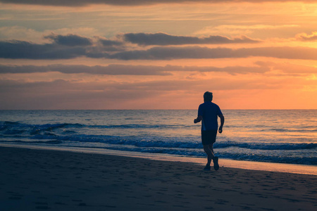 日出时，男人正在海滩边跑步。