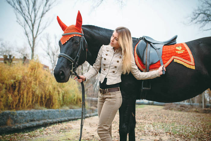 在寒冷的秋日，一个年轻的金发女郎带着一匹马