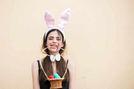 复活节女孩拿着柳条篮子，牙齿上有鸡蛋。 米色背景上有玫瑰色兔子耳朵的女人。 生育和重生的概念。 复活节传统和象征。 春天的节日庆