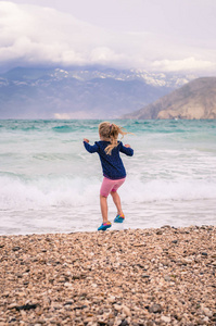 在多风的天气里，充满大海的岩石海滩上，快乐的小跳跃女孩的后景
