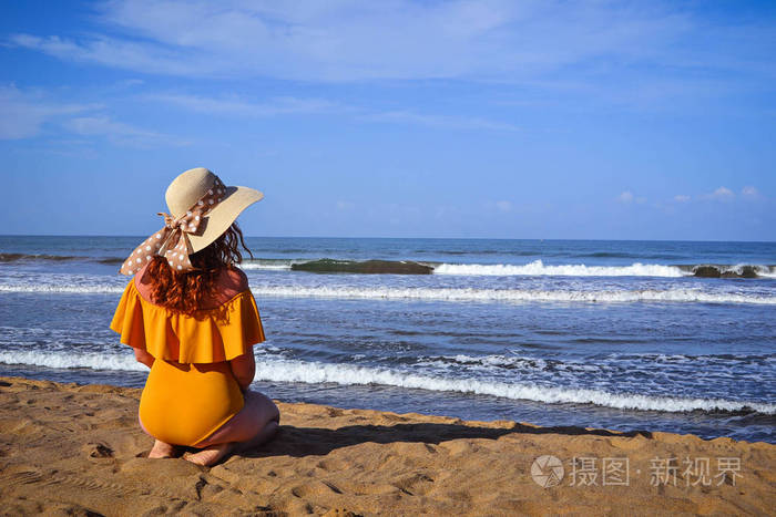 女孩在泳衣和帽子坐在海滩