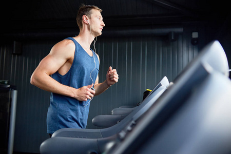 在现代健身运动中，肌肉发达的年轻人在跑步机上跑步的侧视图复制空间