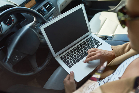 高角度特写无法辨认的成功男人使用笔记本电脑坐在昂贵的汽车复制空间内