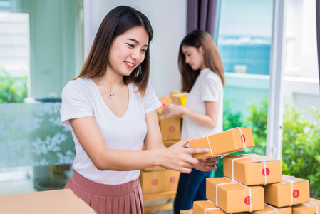 两个年轻的亚洲女孩自由职业者的企业主工作在家里的室和分拣包裹邮政信箱到客户的送货服务。包装订单和购物在线概念