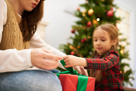 穿着针织背心坐在舒适的客厅地毯上帮小女儿为爸爸包圣诞礼物的女人面目全非