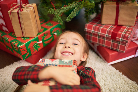 可爱的小女孩摆姿势拍照，躺在舒适的地毯上，拥抱圣诞礼物盒腰部肖像。