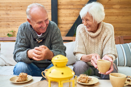 一对幸福的老夫妇在退休时一起欢笑，一起享受时光，坐在户外咖啡馆的桌子上，喝着咖啡和蛋糕