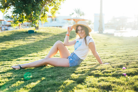 年轻的美女戴着帽子和太阳镜躺在草地上的花园阳光灿烂