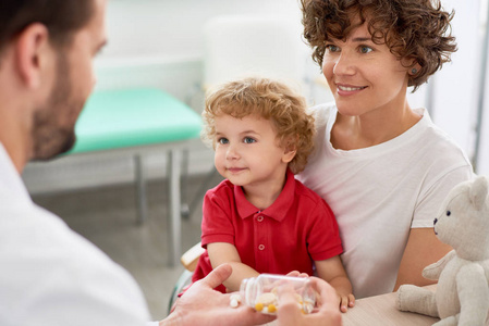 与儿科医生约会时，幸福的母亲和孩子坐在医生办公室，给他们提供维生素