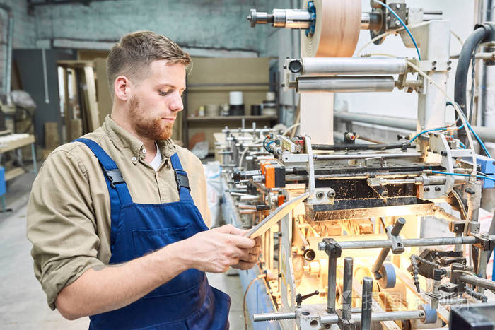 年轻工人在工厂车间使用现代机器的肖像,通过数字平板电脑复制空间