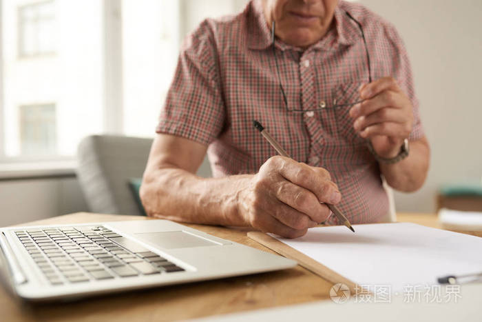 不可辨认的老人在家里用笔记本电脑工作时填写文件