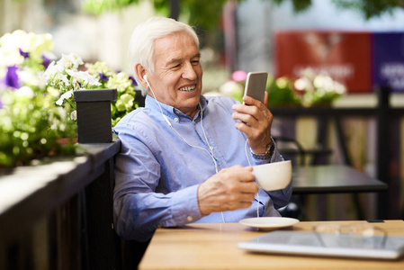 微笑的高级商人在户外咖啡厅休息室使用智能手机视频通话的肖像。