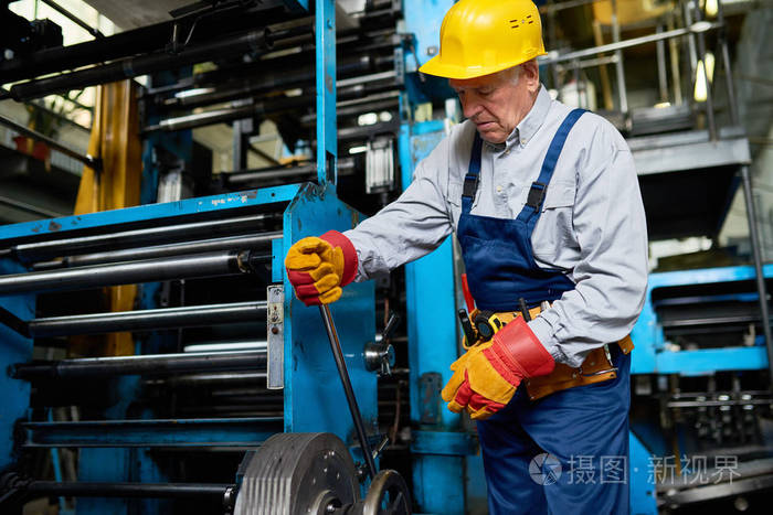 高级工厂工人在车间大机器上切换杠杆的肖像。