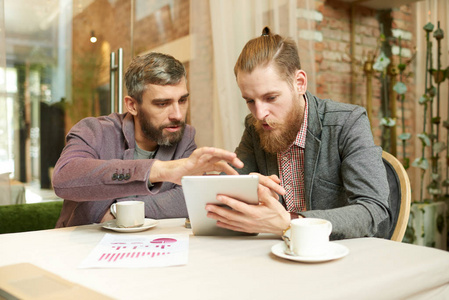 团队辛勤工作的经理使用数字平板电脑，同时在舒适的咖啡屋和时尚的内部进行项目讨论