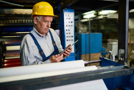 自信成熟的工人穿着硬帽，整体使用数字平板白色，在现代工厂生产部盘点库存。