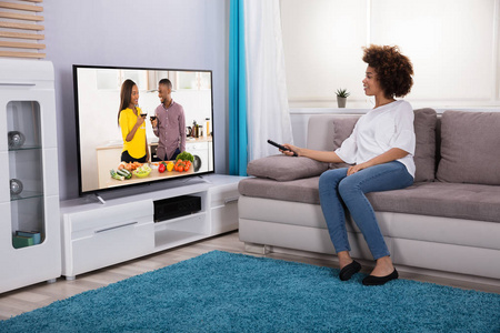 拿着遥控器坐在沙发上拿着遥控器在家看电视的年轻女子照片