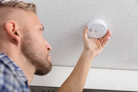 s Hand Installing Smoke Detector On Ceiling Wall At Home