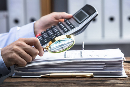 s Hand Using Calculator While Analyzing Bill With Magnifying Gla