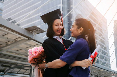 你做到了。 快乐的亚洲母亲抱着鲜花祝贺她的白种人女儿毕业家庭教育自豪的学位证书祝贺仪式和成功的概念