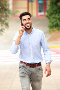 微笑的阿拉伯阿拉伯男子的肖像，走在街上，用手机说话