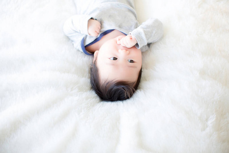 可爱的小男孩正在演播室里拍摄。 婴儿和家庭的时尚形象。 可爱的婴儿躺在柔软的白色地毯上。 背景壁纸图像复制空间物体时尚和文章。