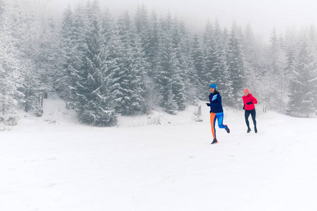 在冬天的山上，女孩们一起在雪地上奔跑。运动，健身的灵感和动力..冬天，两个女伴在山上奔跑。女性跑步者在户外慢跑。