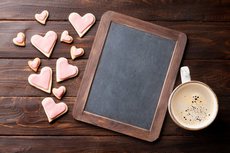 情人节贺卡与心形饼干和咖啡杯在木桌上。 带文字的黑板