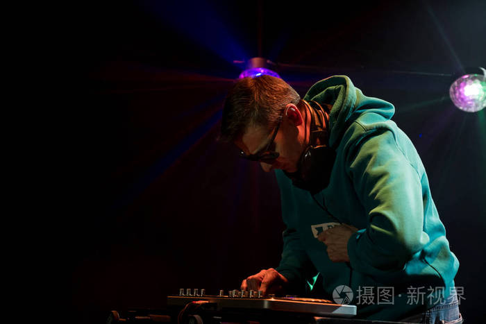 DJ在夜总会工作。 俱乐部里的迪斯科灯。 转盘后面的DJ。
