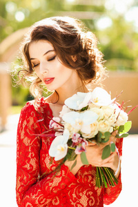 美丽的年轻女子，穿着优雅的红色花边礼服，手捧花束