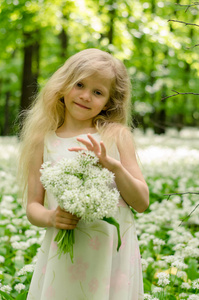 美丽的女孩仙女，金发碧眼，在春天的森林里捧着一束白色的野蒜花