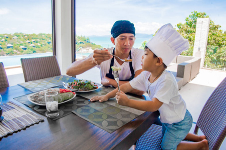泰国男人和他可爱的儿子在家里吃午饭。玩游戏的