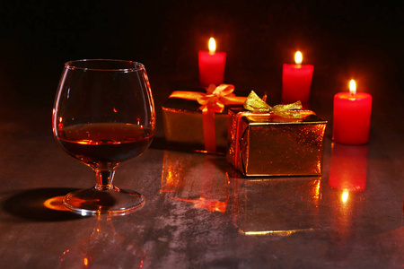 圣诞节装饰。木制背景下的白兰地或威士忌, 红色蜡烛和礼品盒玻璃