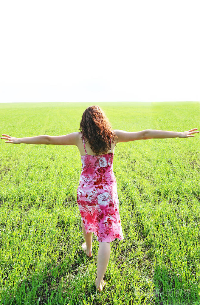 快乐的赤脚女人的后视图长发走在绿草上