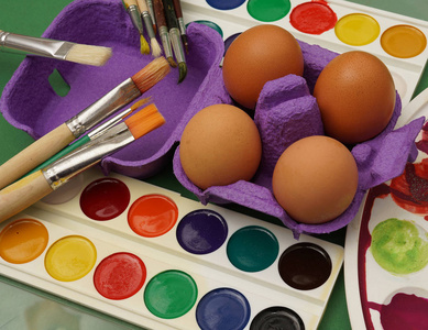 紫罗兰盒里的复活节鸡蛋。 快乐的复活节背景。 绿色桌布背景上的刷子和油漆