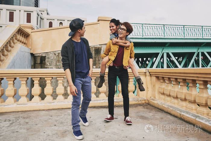 快乐的亚洲青少年背着他漂亮的女朋友一边和他们在城市的朋友散步一边