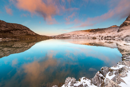 在科瓦东亚阿斯图里亚斯湖的满月前的日落，在那里，冬天的夜晚水中的反射与雪形成了鲜明的对比