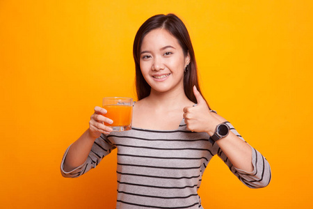 年轻的亚洲女人竖起大拇指喝桔子汁