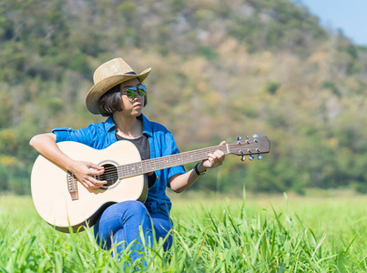 妇女短发戴帽子和太阳镜坐在弹吉他
