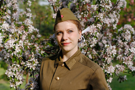 穿二战制服的漂亮的苏联女兵站在开花树附近