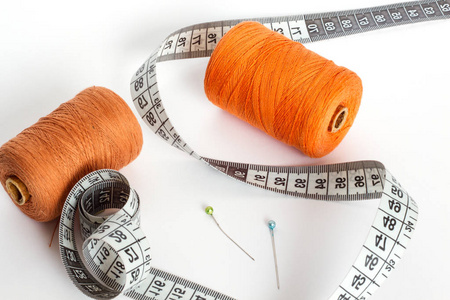 缝制配件 白色背景上的线针和厘米。橙线和棕色的圆筒