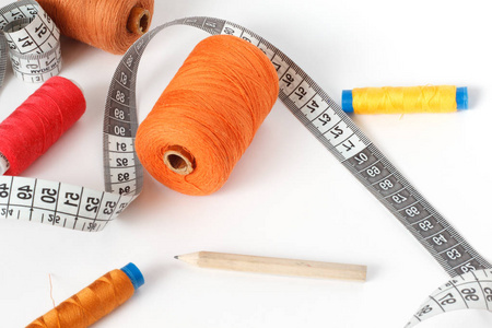 缝纫配件 线, 一支铅笔和一厘米白色背景。橙色, 棕色和红色的筒子线